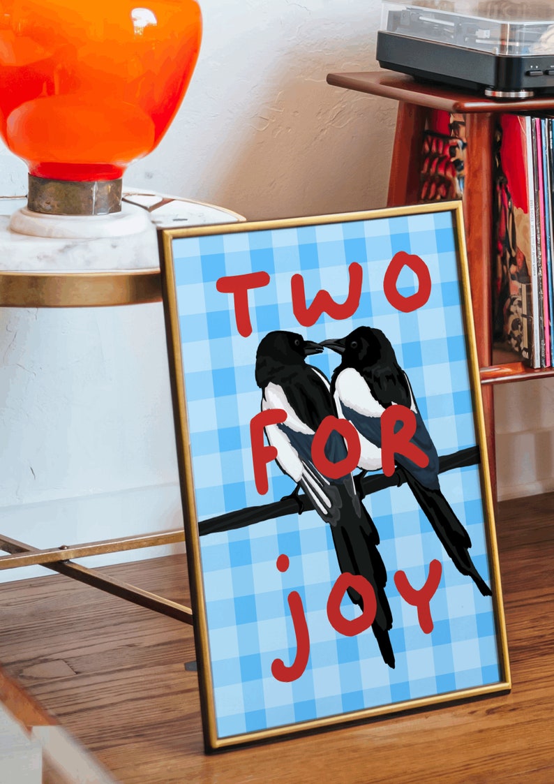 May include: A framed print with a blue and white checkered background. Two black and white magpies are perched on a branch. The text "TWO FOR JOY" is written in red letters.