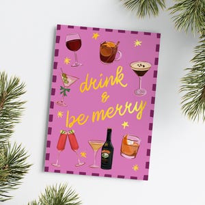 May include: A pink greeting card with the words "drink & be merry" in gold script, surrounded by illustrations of various cocktails and drinks. The card is decorated with small yellow stars and a purple border.