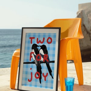 May include: A framed print with a blue and white checkered background featuring two magpies perched on a branch. The text "TWO FOR JOY" is written in red on the print.
