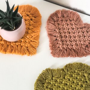 Peut inclure: Trois dessous-de-verre en forme de cœur en crochet avec des franges. Les dessous-de-verre sont dans des tons jaune moutarde, rose poussiéreux et vert olive.
