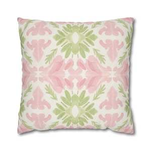May include: Square cushion with a watercolour floral pattern in pink and green on a cream background. The design features symmetrical floral and leaf motifs, creating a soft, artistic look. The cushion is a square shape.