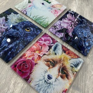 May include: Set of four square coasters featuring colourful floral designs with animal illustrations. The coasters feature a white rabbit, a black raven, a red fox, and a blue owl.