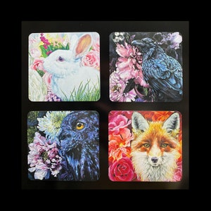 May include: Four square coasters with colorful floral designs and animal illustrations. The coasters feature a white rabbit, a black raven, a blue owl, and a red fox.