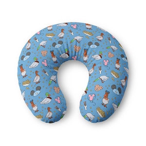 May include: A U-shaped nursing pillow featuring a light blue background with a repeating pattern of ducks, mouse-ear silhouettes, pink balloons, and small containers of french fries. The illustrations are rendered in a colorful, hand-drawn style.