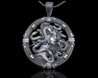 May include: A silver pendant necklace featuring a detailed depiction of Medusa, the Greek mythological figure with snakes for hair. The pendant is circular and has a intricate design with a raised image of Medusa's face surrounded by snakes.