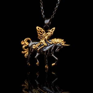 Könnte beinhalten: Eine goldfarbene Fee, die auf einem schwarzen Einhorn reitet, als Anhänger an einer Halskette. Die Fee hat Flügel und hält sich an der Mähne des Einhorns fest. Die Halskette ist an einer schwarzen Kette.