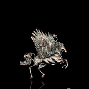 Könnte beinhalten: Ein detaillierter Anhänger aus bronzefarbenem Metall, der ein geflügeltes Pferd, wahrscheinlich Pegasus, darstellt. Das Pferd bäumt sich auf, mit weit ausgebreiteten Flügeln. Der Anhänger hat aufwendige Details und einen schwarzen Hintergrund.