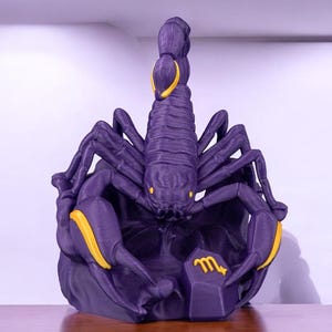 Op de afbeelding: Paarse 3D-geprinte sculptuur van een schorpioen met een gouden sterrenbeeld Schorpioen op een paarse basis.