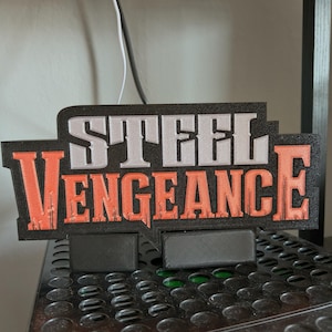Puede incluir: Un letrero negro con las palabras "STEEL VENGEANCE" en letras blancas y naranjas. El letrero está sobre una superficie de metal negro.