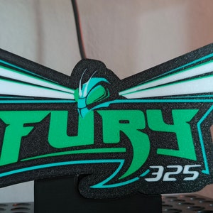 May include: A black, green, and white sign with the word "FURY" in large green letters. The number "325" is below the word "FURY". The sign has a stylized insect head design above the word "FURY".