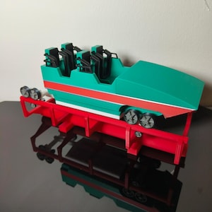 May include: A model roller coaster carriage in teal, with red and white stripes, and black seating. It rests on a red track frame with black wheels. The model is designed for a miniature amusement park and is made of plastic.