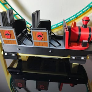 May include: A black and red miniature roller coaster train with wooden seats and a red and black engine. The train is on a yellow and green track.