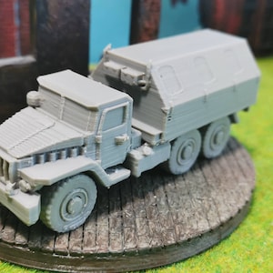 May include: A grey, military-style truck model with a closed cargo bed. The truck has a detailed cab and four wheels.