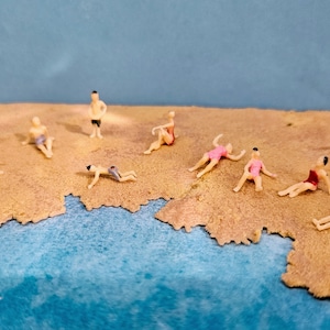 以下が含まれることがあります： 様々なポーズをとった人々のミニチュアビーチシーン。泳いだり、日光浴をしたり、立ったりしています。フィギュアはプラスチック製で、リアルな色で塗装されています。ビーチは砂でできており、水は青いです。