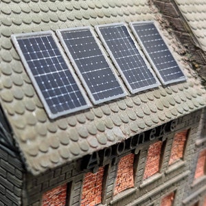 Può includere: Modello in miniatura di un edificio con tetto di tegole grigie e quattro pannelli solari. L'edificio ha muri di mattoni e finestre. La parola "Apotheke" è visibile.