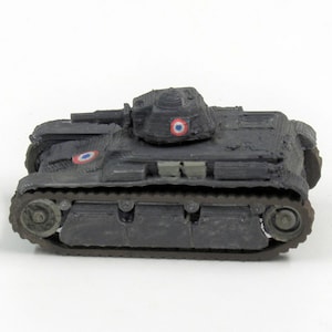 Op de afbeelding: Een zwarte speelgoedtank met een Franse vlag aan de zijkant. De tank heeft een torentje met een kanon en wielen aan de onderkant.