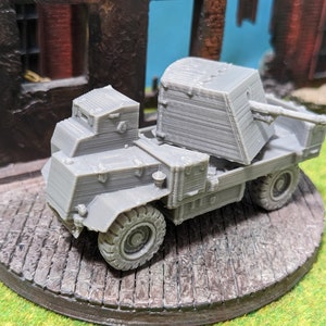 May include: A grey, 3D printed model of a military vehicle with a gun turret mounted on the back. The vehicle has a closed cab and four wheels.