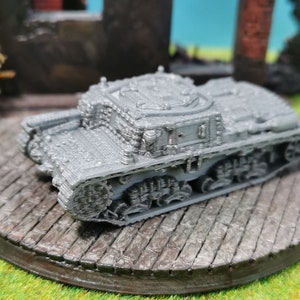 Könnte beinhalten: Ein graues Miniatur-Panzermodell mit detaillierten Ketten und einer strukturierten Oberfläche. Der Panzer steht auf einer kreisförmigen, steinartigen Plattform, mit einem Hintergrund aus grüner Oberfläche und einem verschwommenen, kriegszerstörten Gebäude.