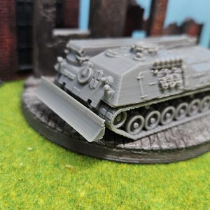 Könnte beinhalten: Ein graues Plastikmodell eines militärischen gepanzerten Fahrzeugs mit einem Bulldozer-Blatt. Das Fahrzeug hat ein detailliertes Design mit Ketten und einem erhöhten Turm.