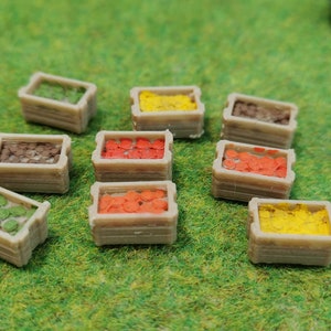 Può includere: Nove cassette di legno in miniatura riempite con materiali artigianali di diversi colori. Le cassette sono disposte a semicerchio su una superficie verde. I materiali includono verde, arancione, giallo e marrone.