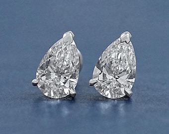 May include: A pair of pear-shaped diamond earrings set in a silver metal setting. The earrings are on a blue background.
