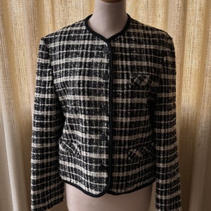 May include: A black and white plaid blazer with a black trim. The blazer has a button closure and is on a wooden mannequin.
