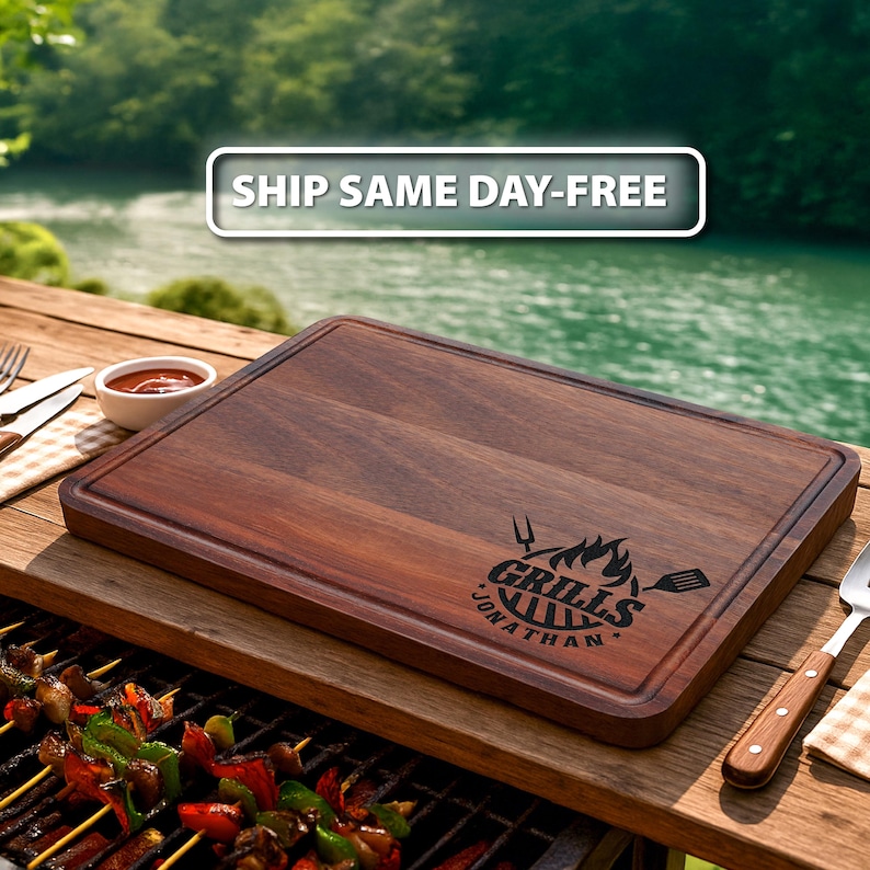Puede incluir: Tabla de cortar rectangular de madera marr&oacute;n oscuro. La tabla tiene una ranura tallada alrededor del borde y un gr&aacute;fico negro que dice "Grills Jonathan". Una parrilla con brochetas de verduras est&aacute; en primer plano.