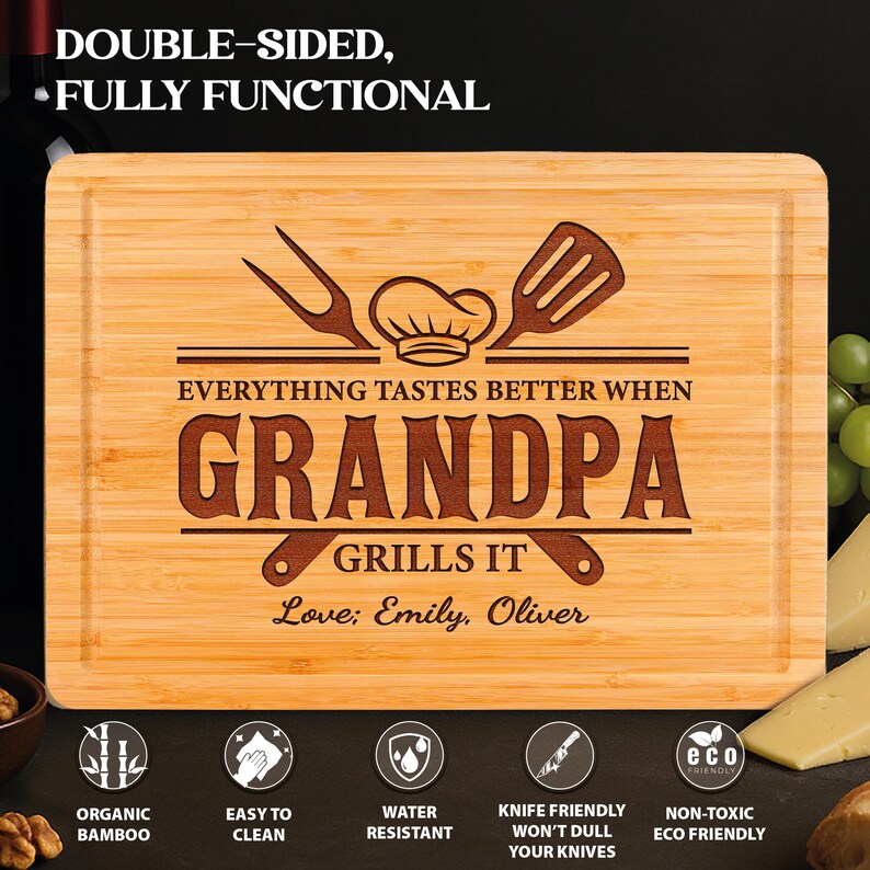 May include: A rectangular bamboo cutting board with a chef's hat, fork, and spatula design. The text reads "EVERYTHING TASTES BETTER WHEN GRANDPA GRILLS IT" with "Love; Emily, Oliver" below. The board is double-sided and fully functional.