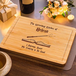 May include: A rectangular bamboo cutting board with a carved juice groove. The board features the text "The Wizarding Kitchen of Helena" and the phrase "I Solemnly Swear My Cooking Is So Good" along with illustrations of a wand and an open book.