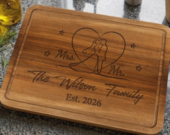 Könnte beinhalten: Ein rechteckiges Holzschneidebrett mit Saftrille, graviert mit einem Herz, das die Silhouette eines Brautpaares enthält, dem Text Mrs. und Mr., The Wilson Family sowie Est. 2026, umgeben von vier kleinen Sternsymbolen.