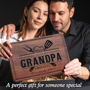 May include: A rectangular wooden cutting board with a dark brown finish. The board is engraved with the words "EVERYTHING TASTES BETTER WHEN GRANDPA GRILLS IT" and includes a chef's hat, spatula, and fork design. The names "Emily, Oliver" are also engraved.