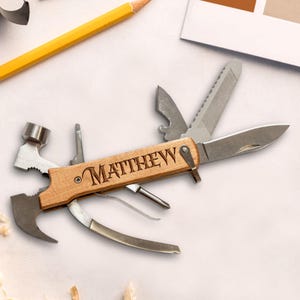 K&ouml;nnte beinhalten: Ein Holz-Multitool mit verschiedenen Werkzeugen, darunter ein Hammer, ein Messer und eine Feile. Der Name "MATTHEW" ist auf dem Holzgriff eingraviert. Ein gelber Bleistift und Farbmuster sind im Hintergrund.