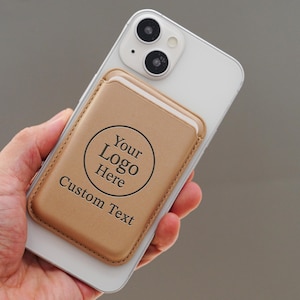 May include: A tan leather phone wallet with a circular logo area and the words "Your Logo Here" and "Custom Text" printed on it. The wallet is attached to a white smartphone.