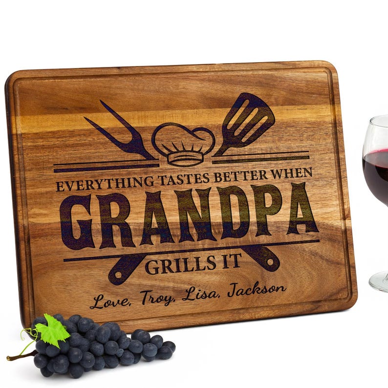 May include: Wooden cutting board with the text "Everything tastes better when Grandpa grills it." Includes a chef's hat, spatula, and fork design. Features the names "Love, Troy, Lisa, Jackson." A bunch of grapes and a glass of red wine are also in the image.