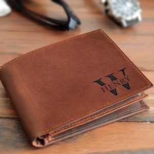 May include: Brown leather wallet with the name "HENRY" and a stylized "W" engraved on the front. The wallet is folded and appears to be new. The stitching is visible around the edges.