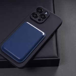 May include: A black smartphone with a blue leather card holder attached. The phone has three camera lenses and is resting on a dark surface. The card holder is rectangular with white trim.