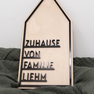 May include: A wooden house-shaped sign with black lettering that reads "Zuhause von Familie Liebhm".