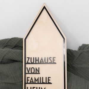 May include: A wooden house-shaped sign with black lettering that reads "ZUHAUSE VON FAMILIE LIEHM".
