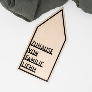 May include: A wooden house-shaped sign with black lettering that reads "Zuhause von Familie Liebhm".