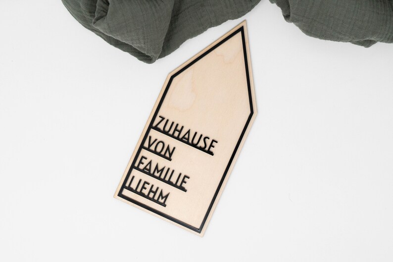 May include: A wooden house-shaped sign with black lettering that reads "Zuhause von Familie Liebhm".