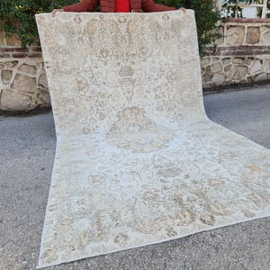 May include: A large, rectangular rug with an intricate, floral pattern in cream and brown tones. The rug is displayed outdoors, showcasing its size and design. The detailed pattern adds a touch of elegance.