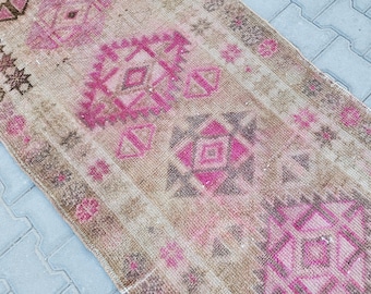 May include: A vintage Turkish rug with a faded pink and brown geometric pattern. The rug has a distressed look and is made of wool.