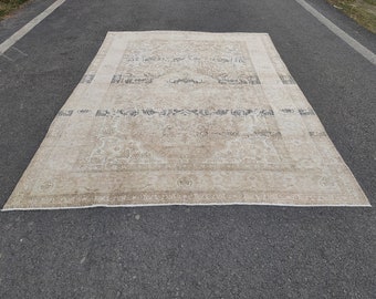 May include: A vintage cream-colored rug with a faded floral pattern and a dark brown border. The rug has a worn and distressed look, giving it a rustic and antique feel.