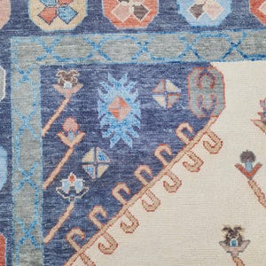 May include: A close-up of a blue and cream patterned rug with intricate floral designs. The rug has a border of blue and cream, and the center is a cream color with a blue floral pattern.