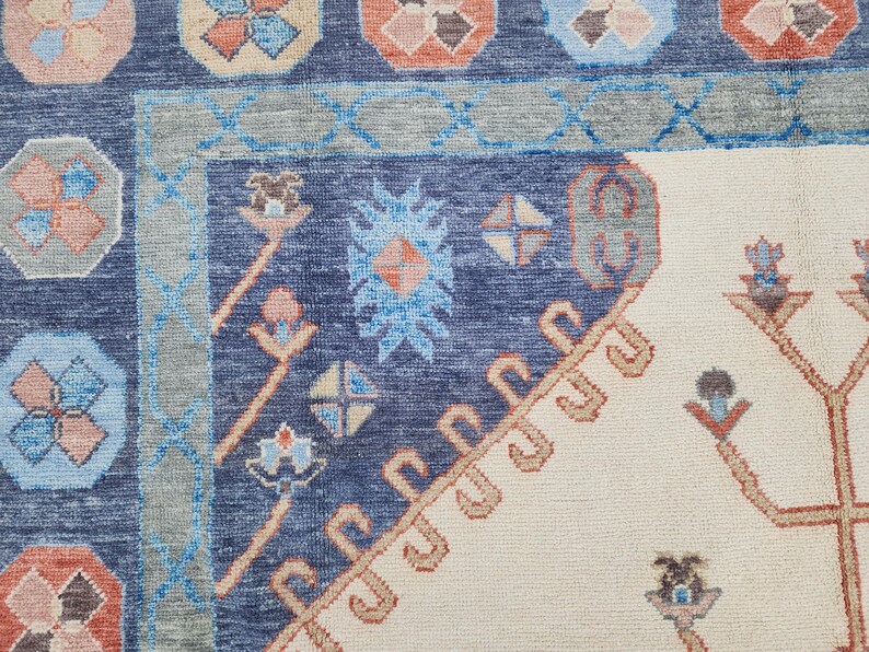 May include: A close-up of a blue and cream patterned rug with intricate floral designs. The rug has a border of blue and cream, and the center is a cream color with a blue floral pattern.