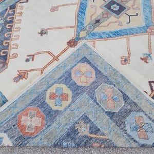 May include: Close-up of a corner of a rug with a cream background and a blue, red, and yellow geometric pattern.