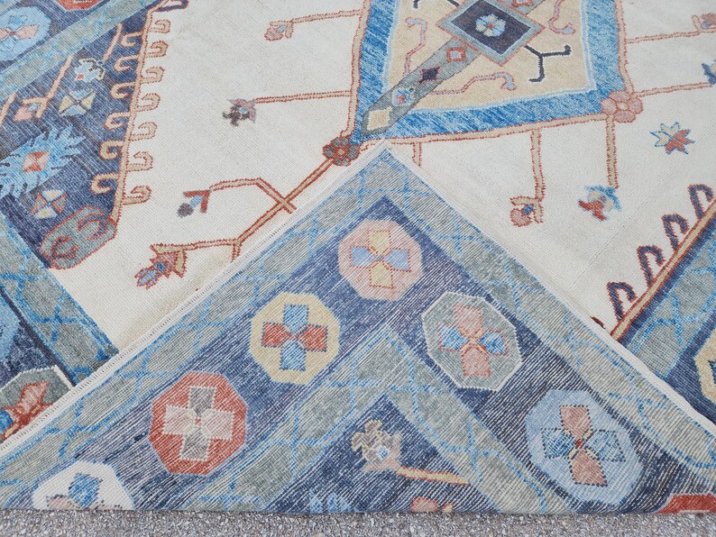 May include: Close-up of a corner of a rug with a cream background and a blue, red, and yellow geometric pattern.