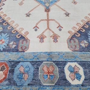 May include: Close-up of a rug with a blue and white border and a central design of a stylized tree with red and white accents.