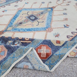May include: A vintage rug with a cream background and a blue, red, and beige geometric pattern. The rug has a fringed edge and is folded in half.