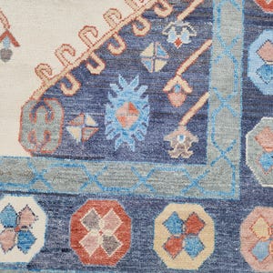 May include: Close-up of a blue and cream rug with a geometric pattern. The rug has a border of blue and cream, and the center is filled with a repeating pattern of flowers and leaves.